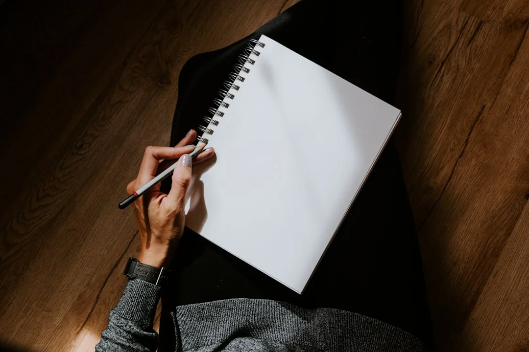Hand writing with a pen in a spiral notebook resting on a lap