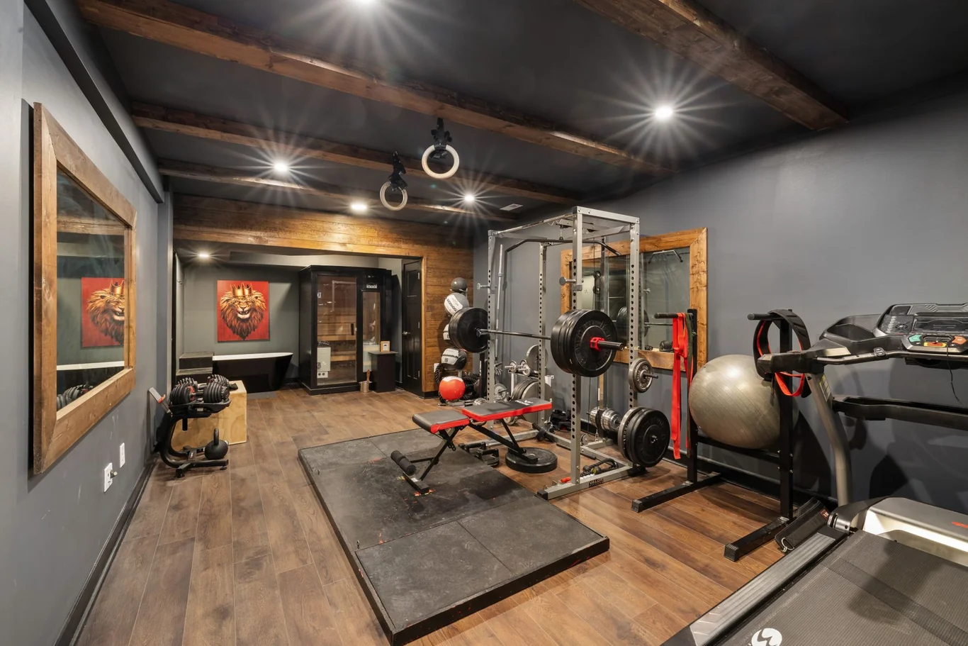 Home gym room with a squat rack, bench, kettlebell, and treadmill under wood beams