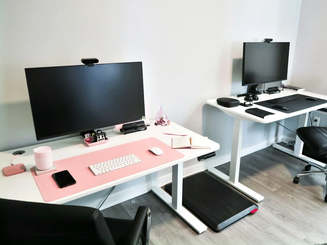 Home office with two standing desks and a walking pad placed under the right workstation