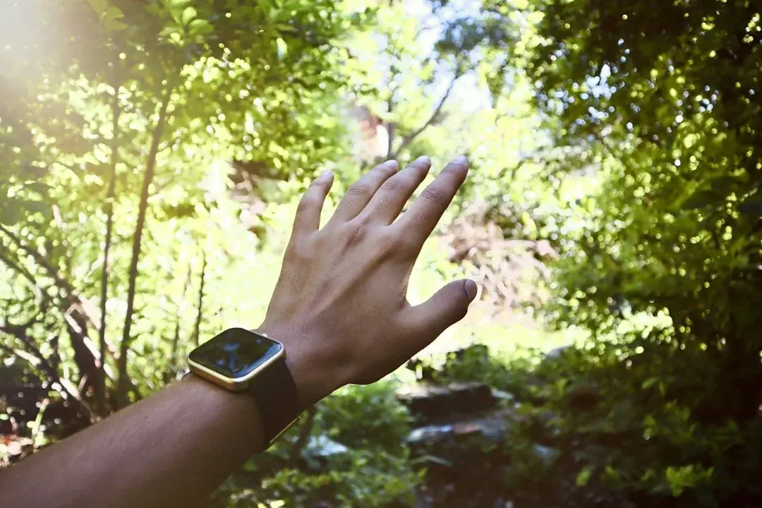 Woman wearing a yellow smartwatch outdoors with sunlit green trees in the background