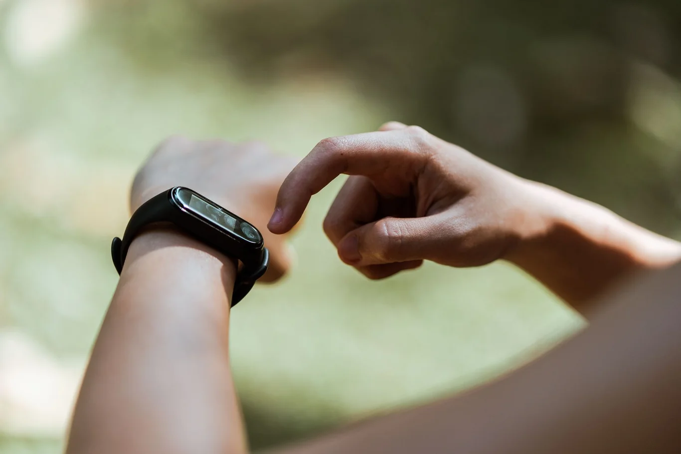 Person tapping a black fitness tracker on their wrist outdoors to check recovery data
