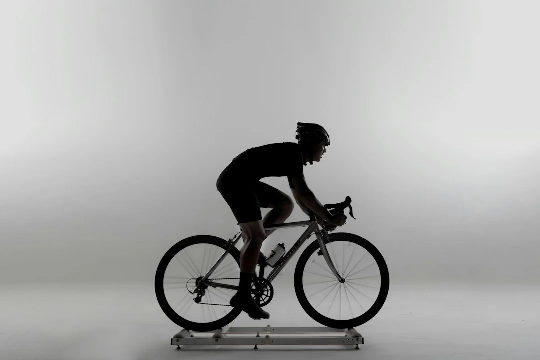 Cyclist in silhouette riding a road bike on indoor training rollers against a gray background