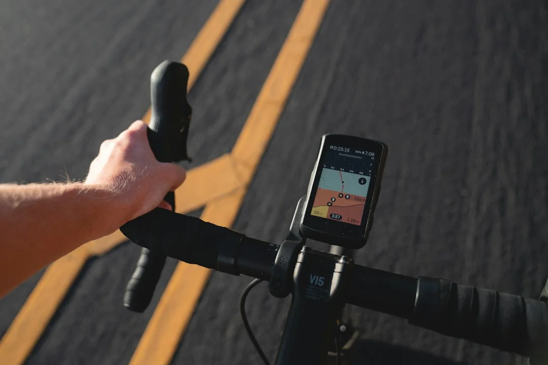 Cyclist gripping handlebars with a GPS computer displaying power and heart rate data on a road