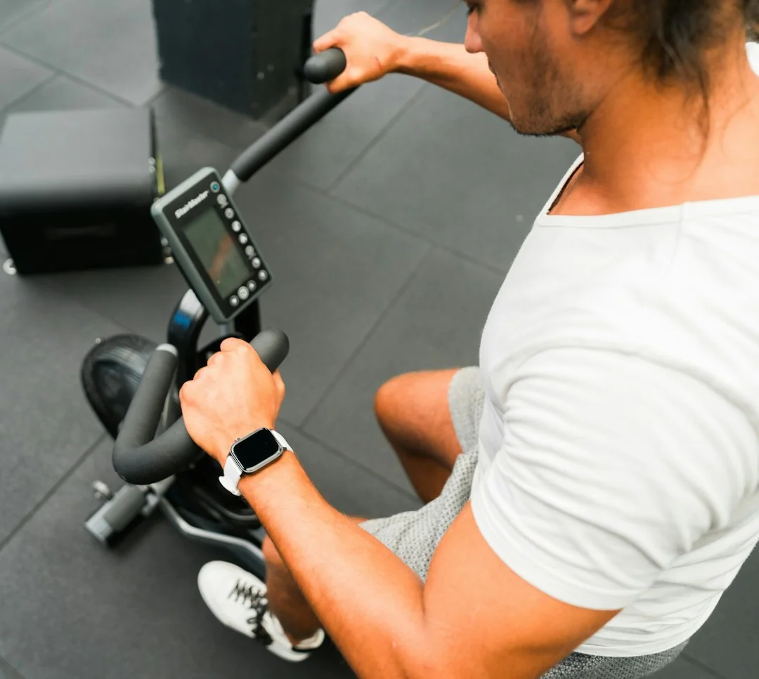 Man on rowing machine in gym pulling handle wearing white shirt and smartwatch