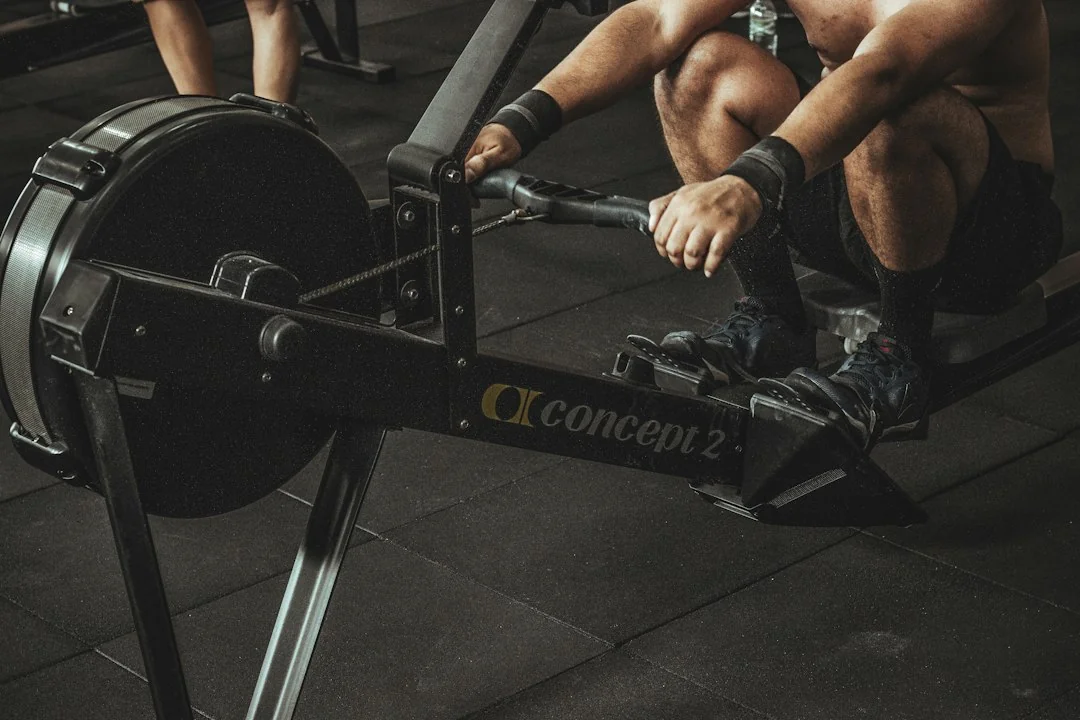 Man gripping Concept2 rowing machine handle in catch position on gym floor