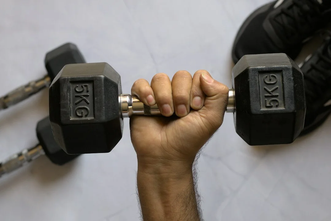 Hand gripping a 5KG hex dumbbell on a white marble floor