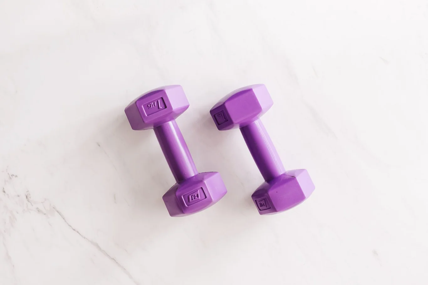 Pair of purple hex dumbbells resting on a white marble surface