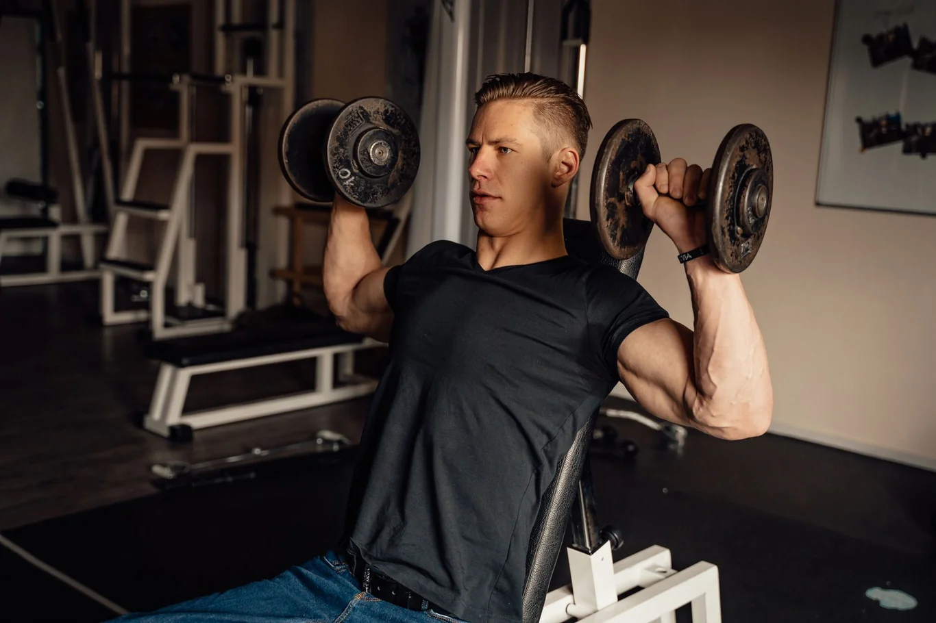 Man performing seated dumbbell shoulder press in a home gym setup