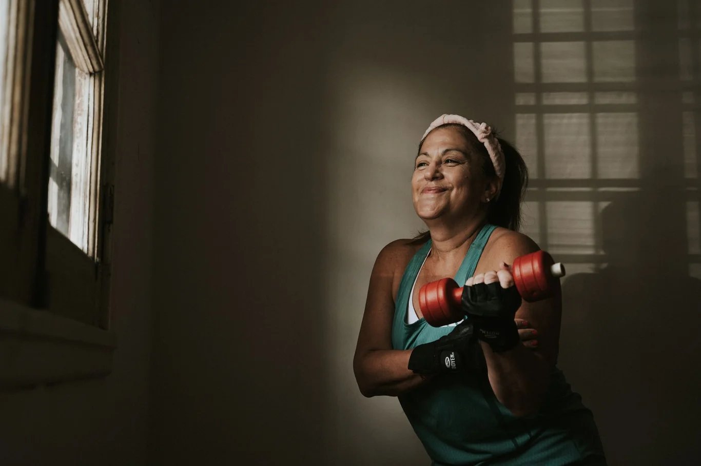 Woman smiling while doing a dumbbell curl near a sunny window at home