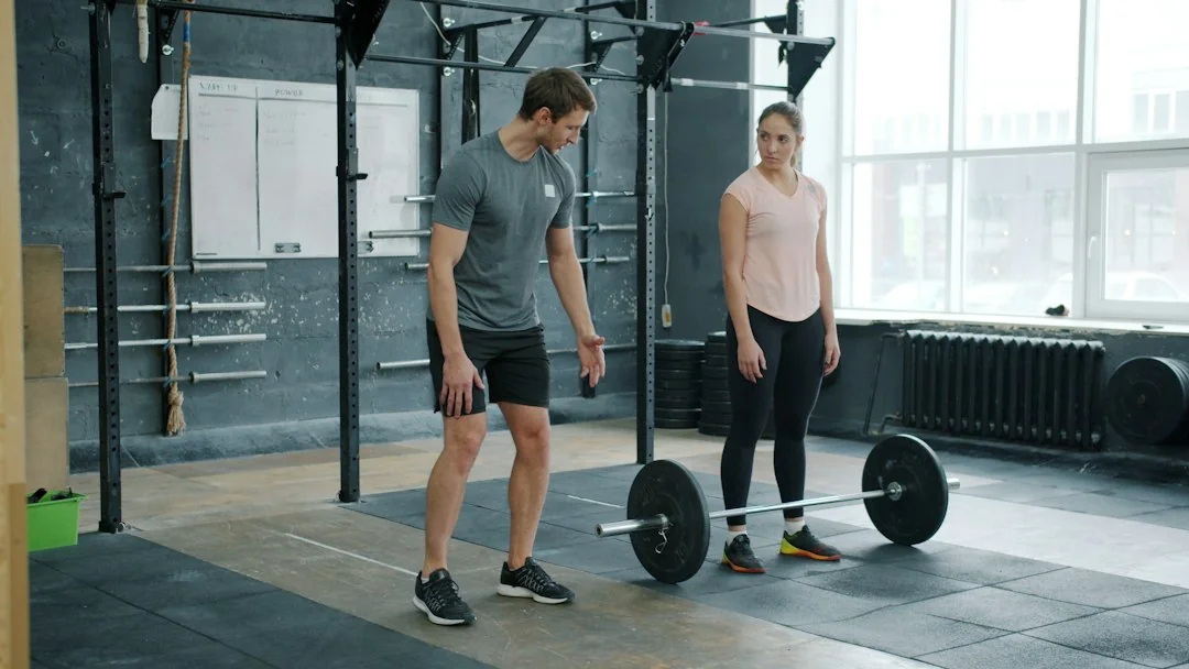 Man preparing to deadlift a barbell while a woman coaches him in a minimalist strength training gym
