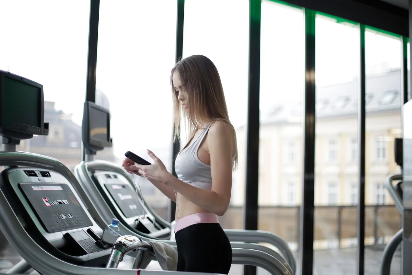 Woman walking on a treadmill in a bright gym with floor-to-ceiling windows