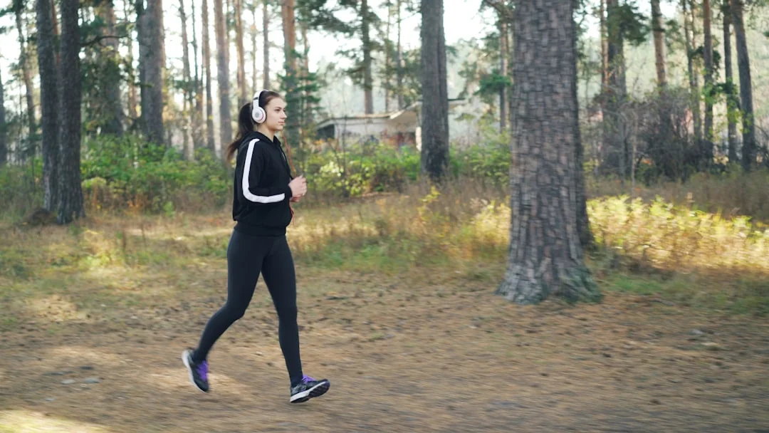 Woman in black athletic wear power walking on a forest trail with headphones