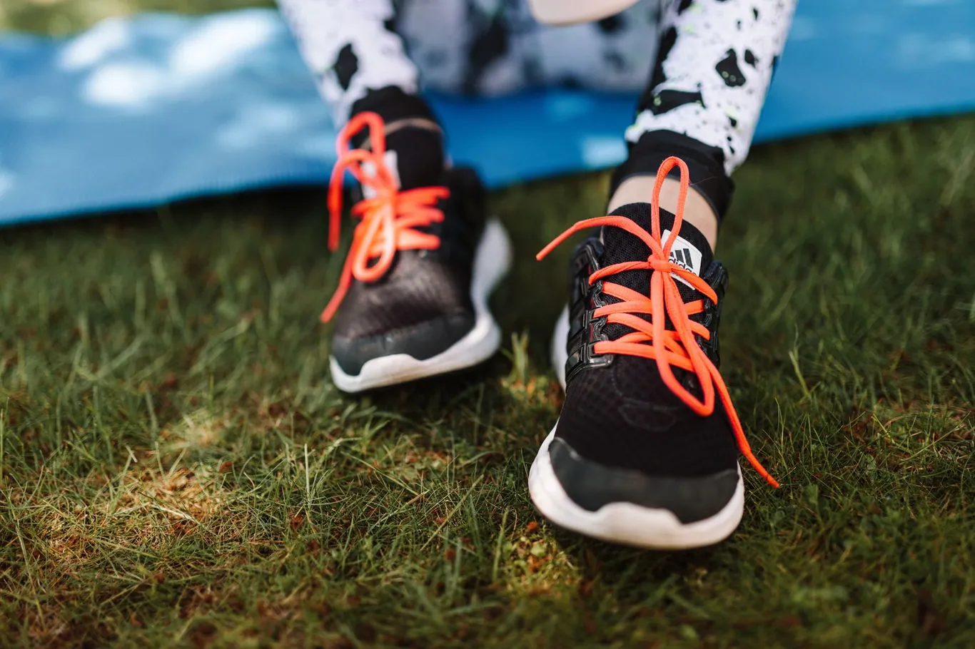Black athletic shoes with orange laces resting on green grass outdoors