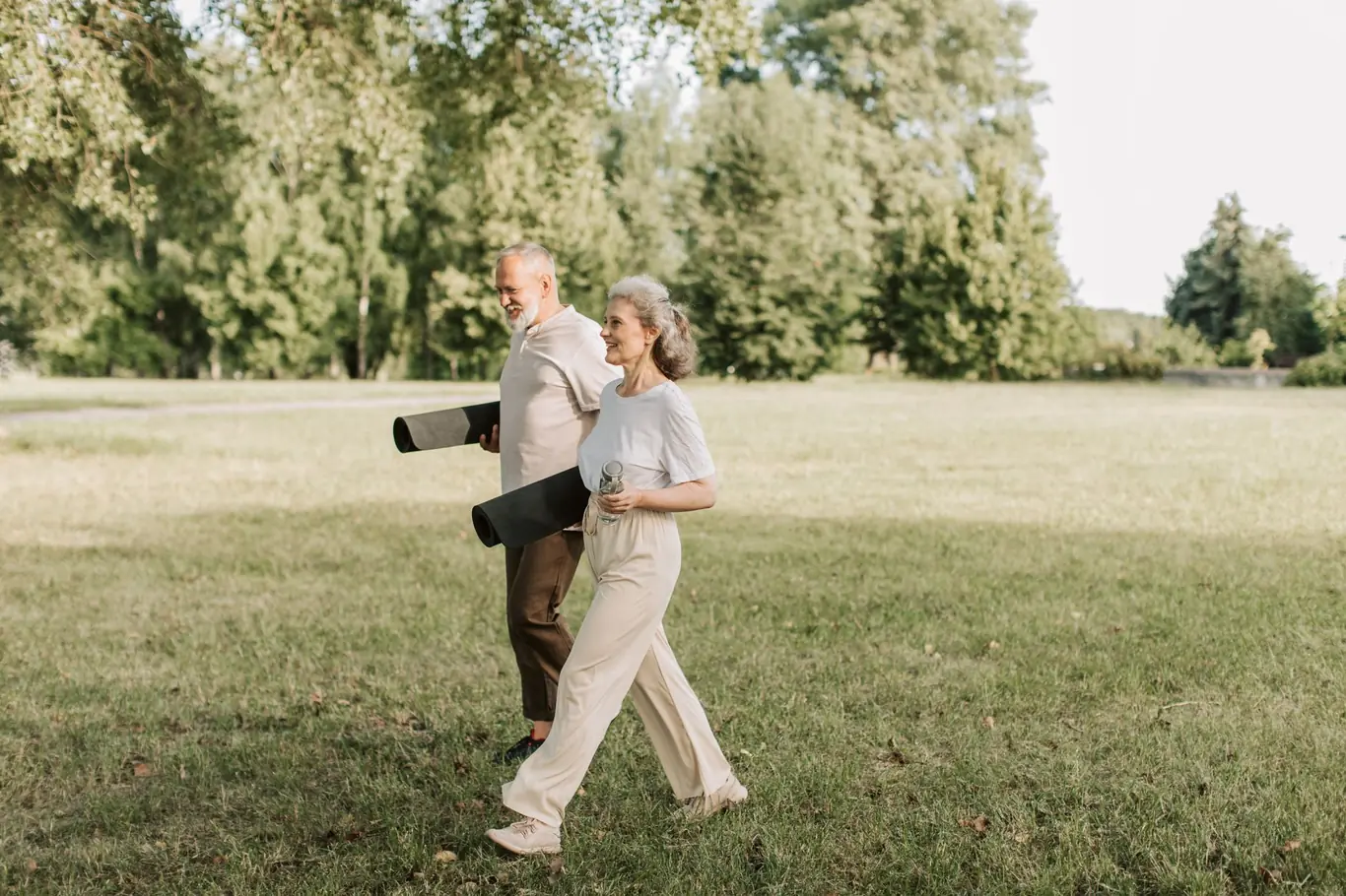Older couple walking together across a green park lawn with trees in background