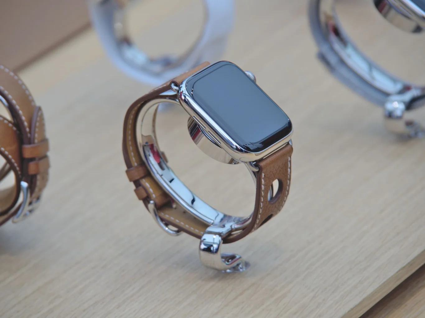 Apple Watch with tan leather band displayed on a wooden retail surface