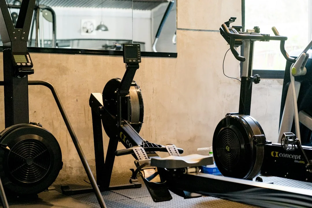 Two rowing machines showing flywheel resistance mechanisms and steel rail construction in a gym