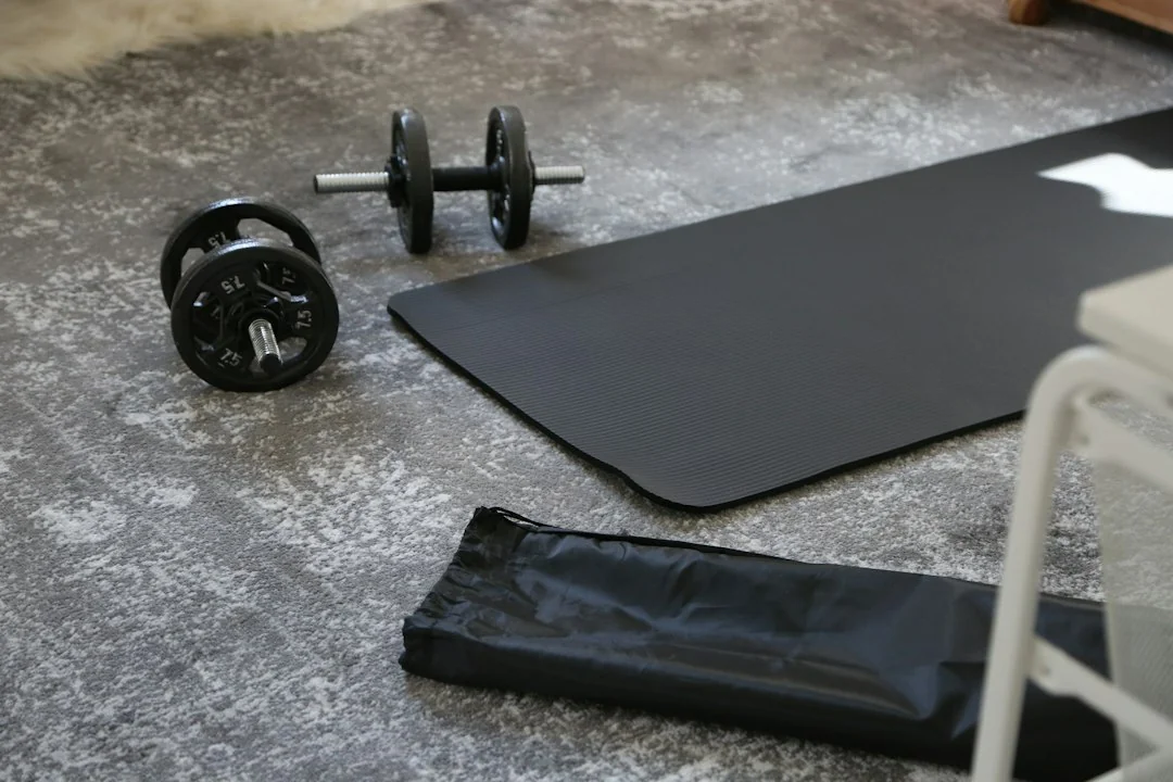 Dumbbells and an exercise mat on a concrete floor next to fitness equipment in a home gym
