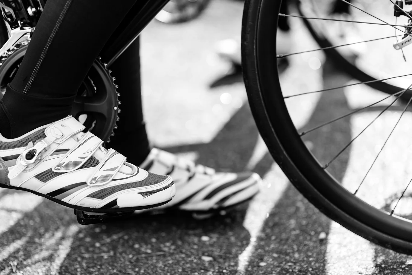 Cyclist wearing white cycling shoes clipped into bike pedals, close-up black and white shot