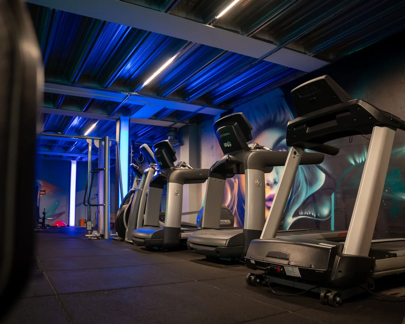 Row of commercial treadmills lined up in a dark gym with blue overhead lighting