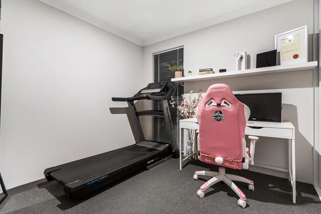 Treadmill set up in a small home office room alongside a desk and gaming chair