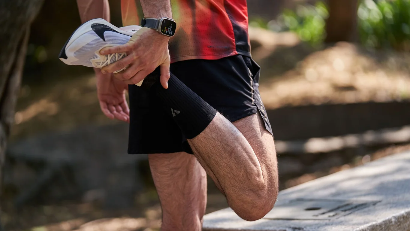 Runner outdoors in a park wearing a smartwatch, stretching after a trail run