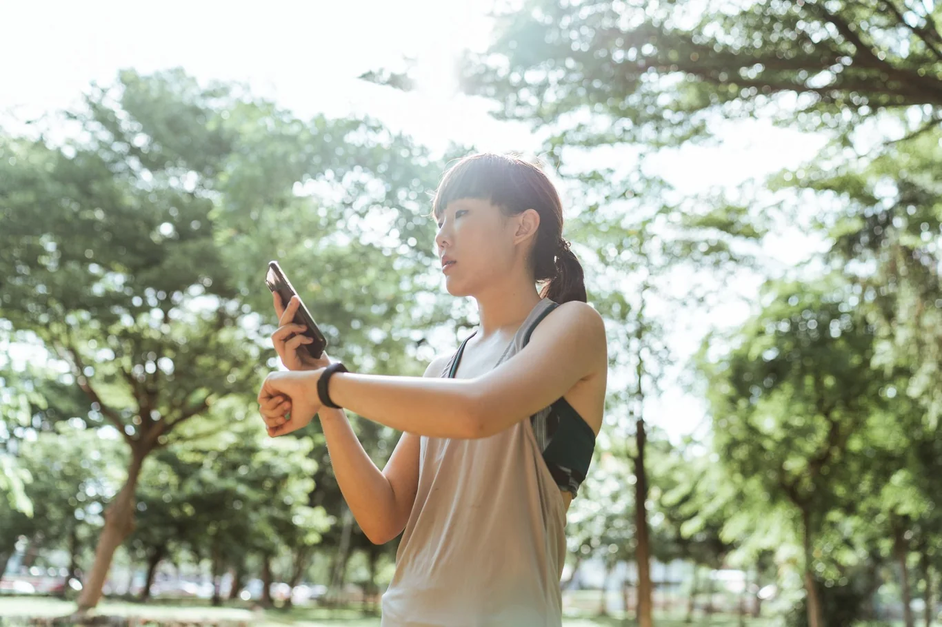 Woman in athletic wear checking her smartwatch and phone while outdoors in a park