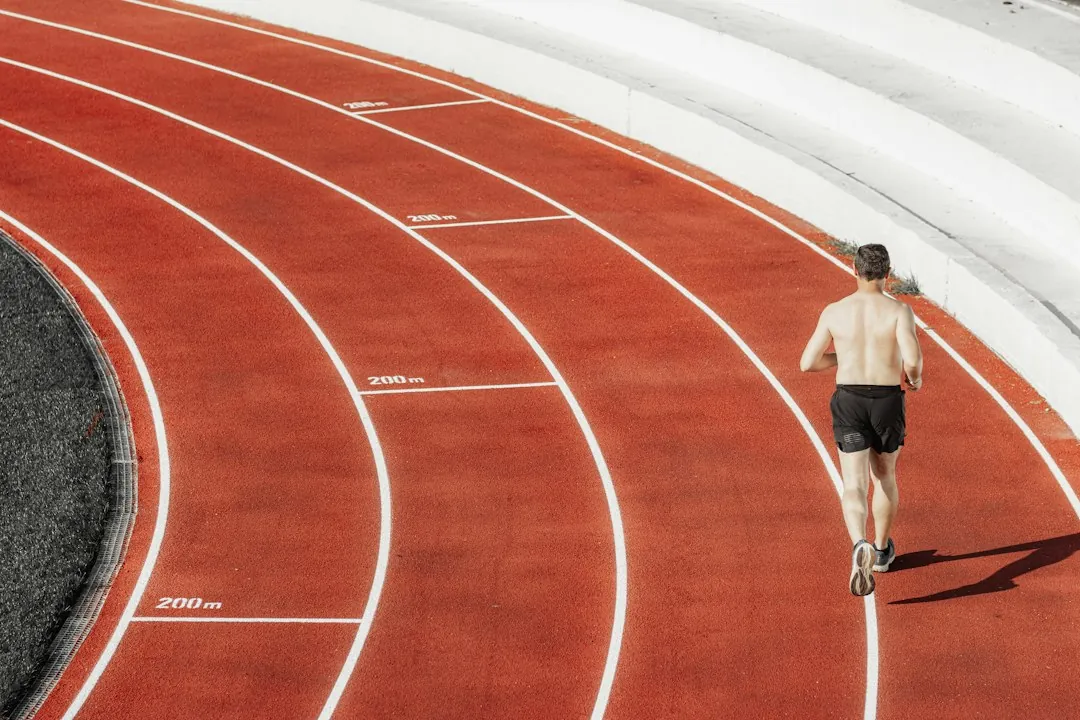 Male runner sprinting alone on a red athletic track during interval training