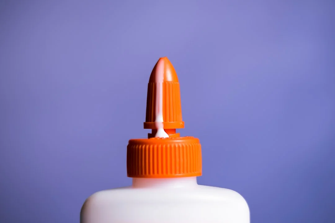 White squeeze bottle with an orange pointed nozzle tip against a purple background