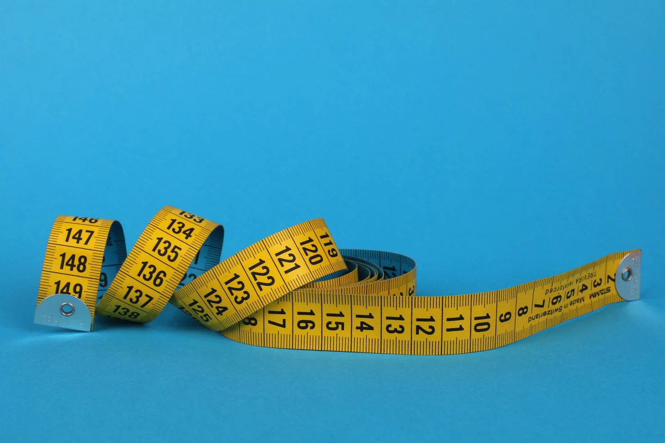 Yellow fabric measuring tape coiled on a blue surface showing numbered length markings