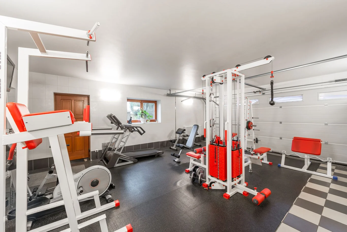 Home gym with treadmill and cable machines set up in a garage
