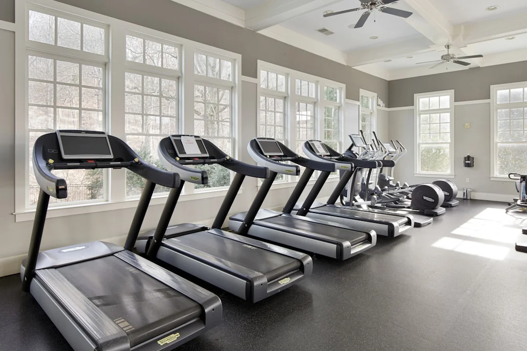 Row of treadmills in a bright home gym with large windows and ceiling fan
