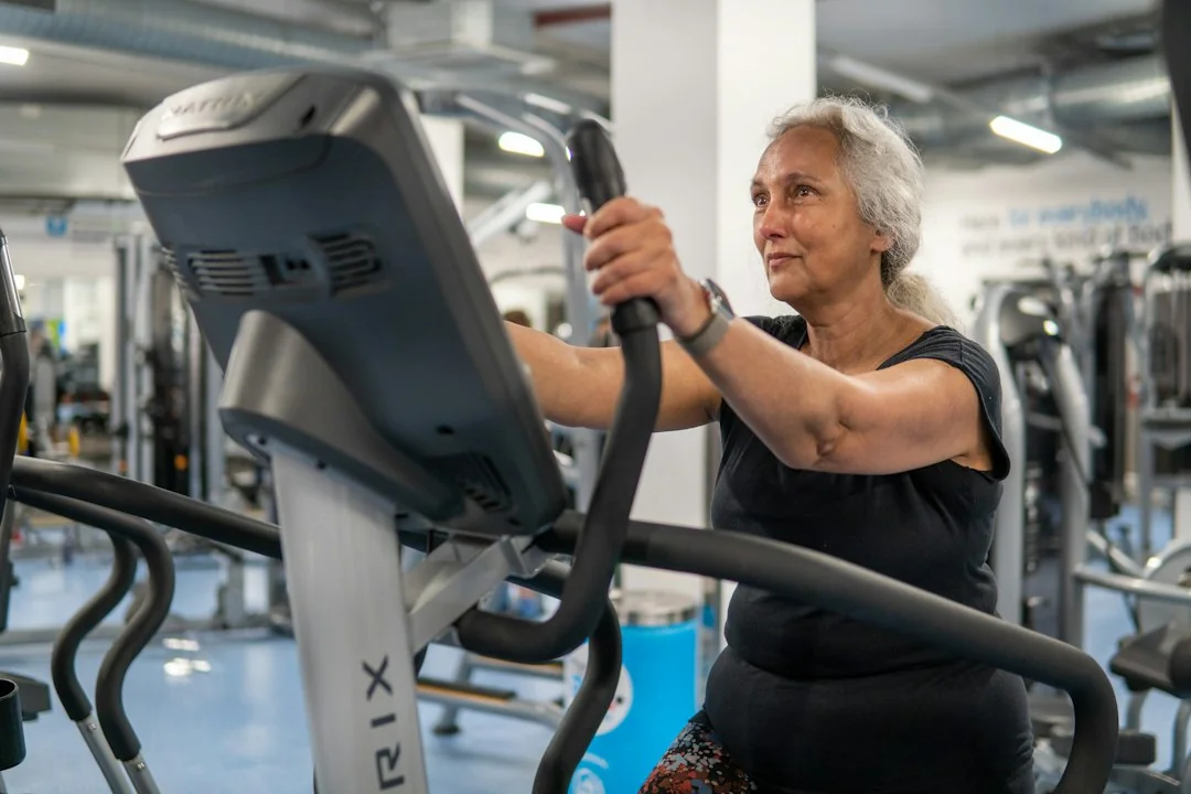 Older woman gripping moving handles on a Matrix elliptical machine in a gym