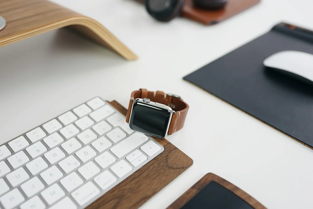 Smartwatch with brown leather band on a white desk beside a keyboard and mouse