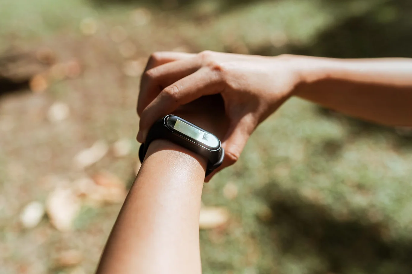 Person checking a slim fitness tracker on their wrist outdoors in natural sunlight