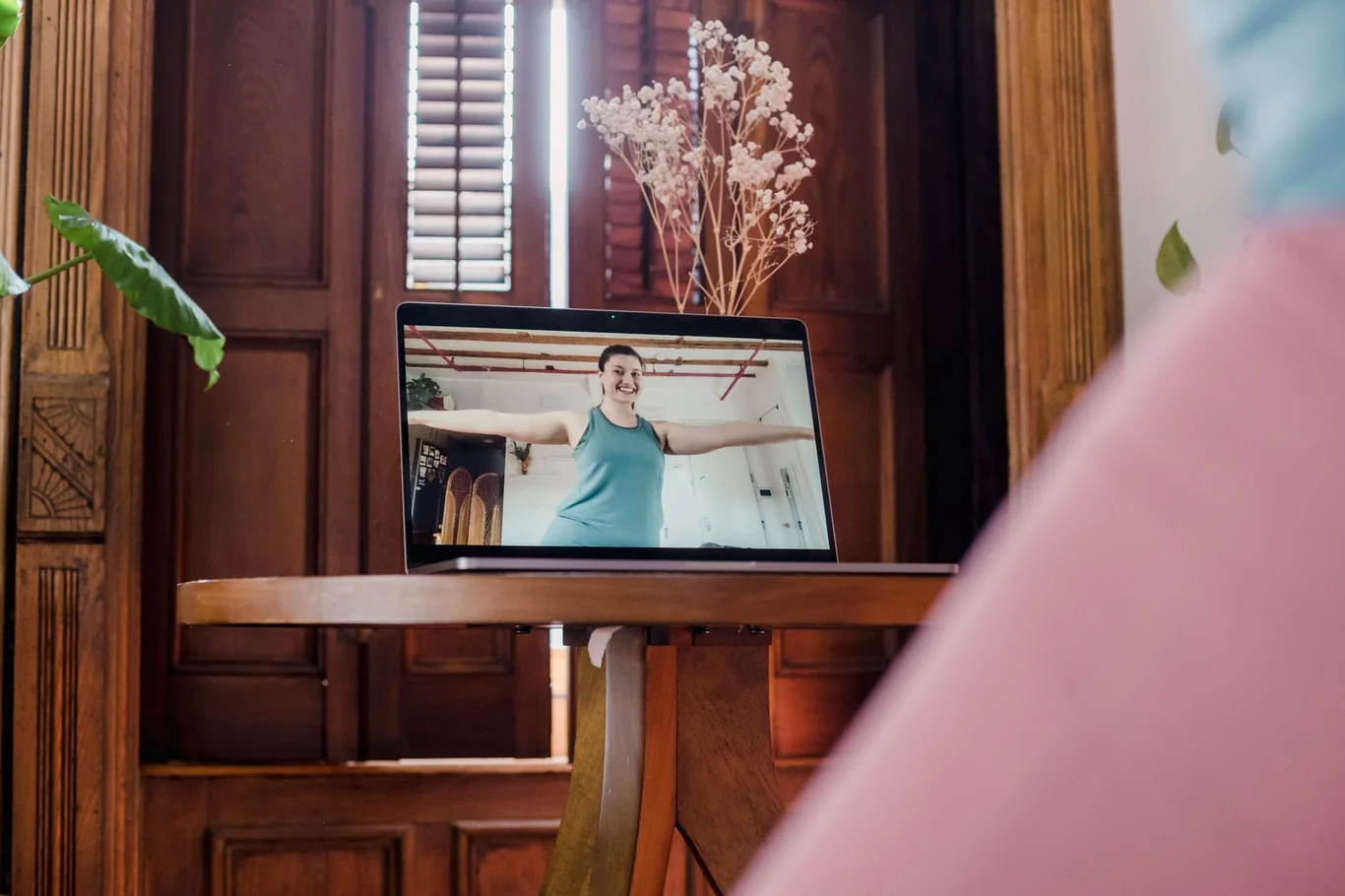A person watches a fitness instructor demonstrate a move on a laptop screen
