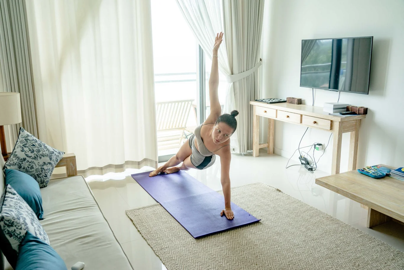 Person holding a side plank pose on a yoga mat near a wall-mounted TV screen