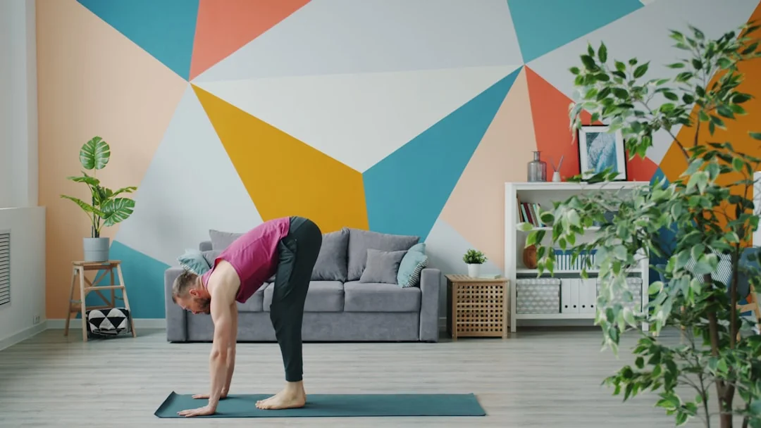 Woman doing a standing forward stretch on a yoga mat in a bright living room