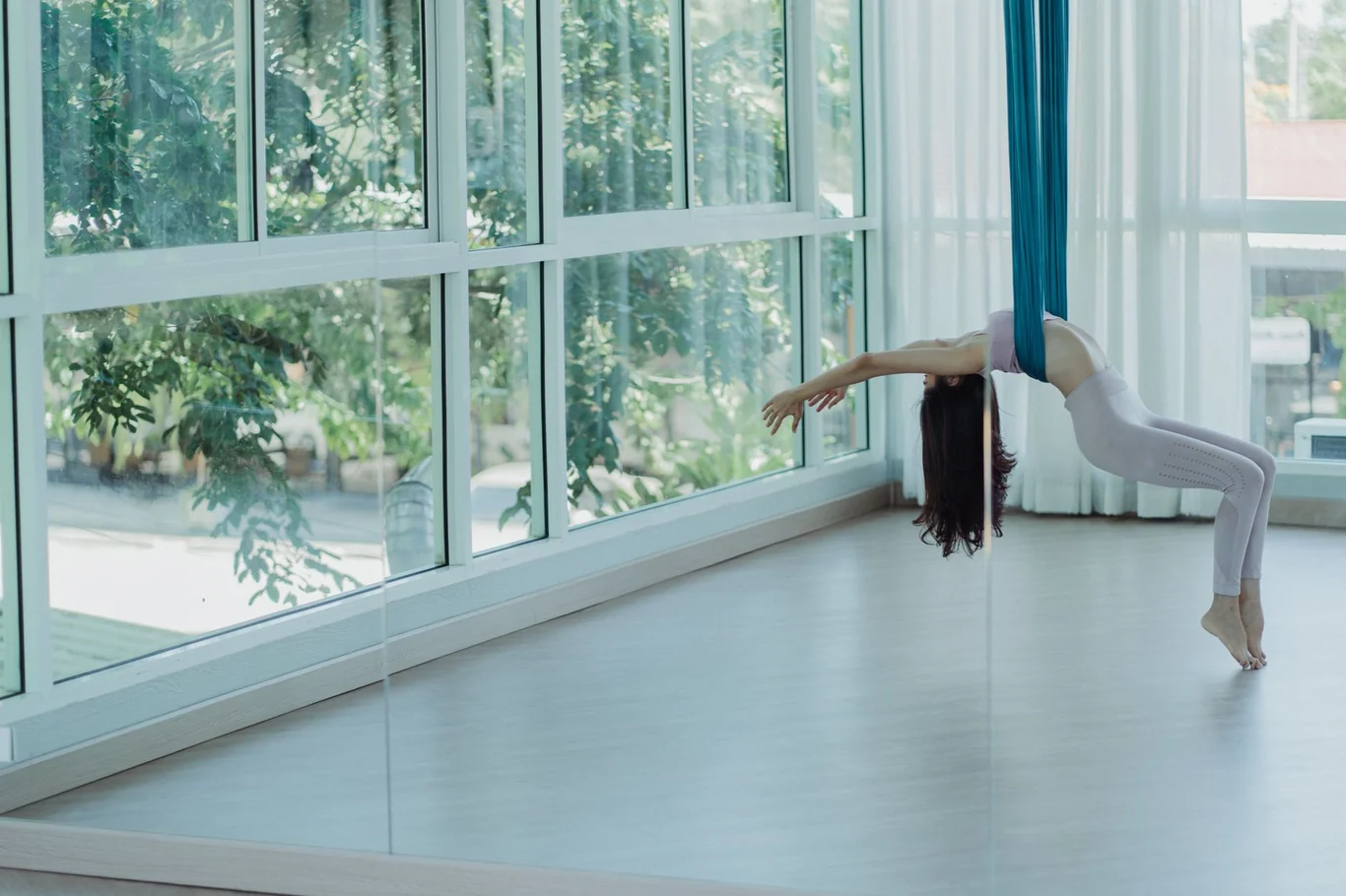 Woman using an aerial yoga hammock stretch in front of a full length studio mirror