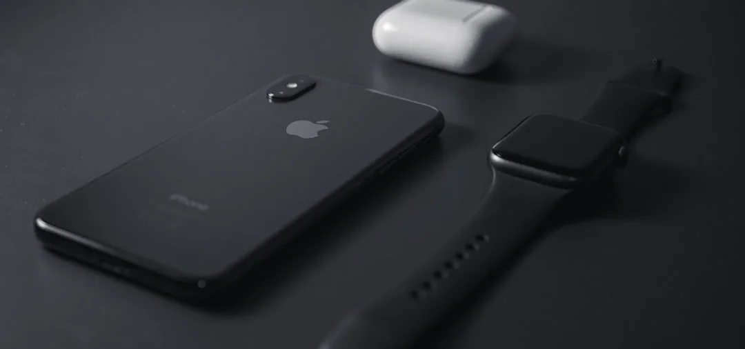 Apple Watch and iPhone resting on a dark surface with AirPods in the background