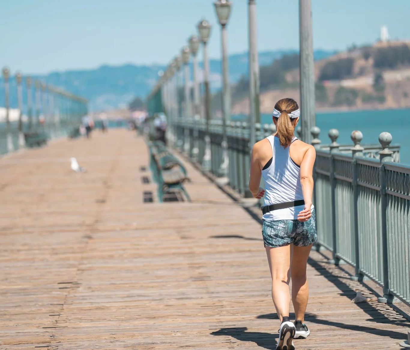 Woman in workout attire walking along a sunny waterfront pier