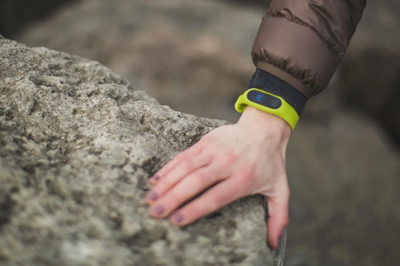 Person wearing a bright green fitness tracker band resting their hand on a stone surface outdoors