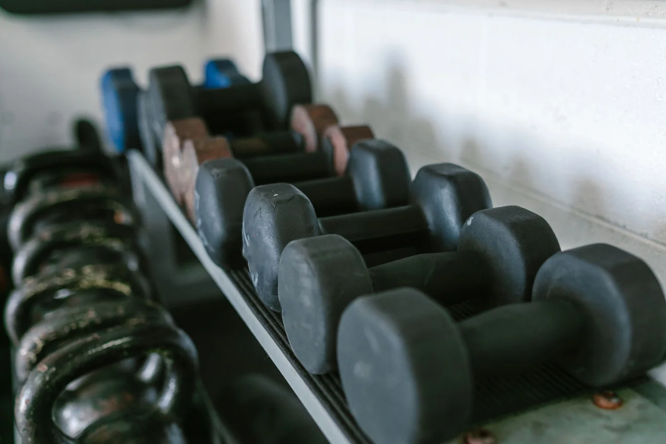 Rack of rubber-coated dumbbells in ascending sizes stored against a garage wall