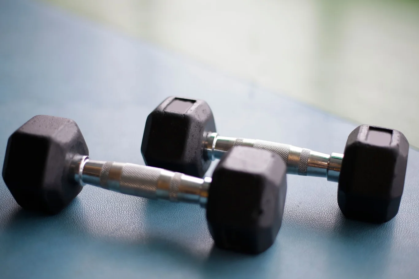 Two rubber hex dumbbells with chrome handles resting on a blue home gym floor