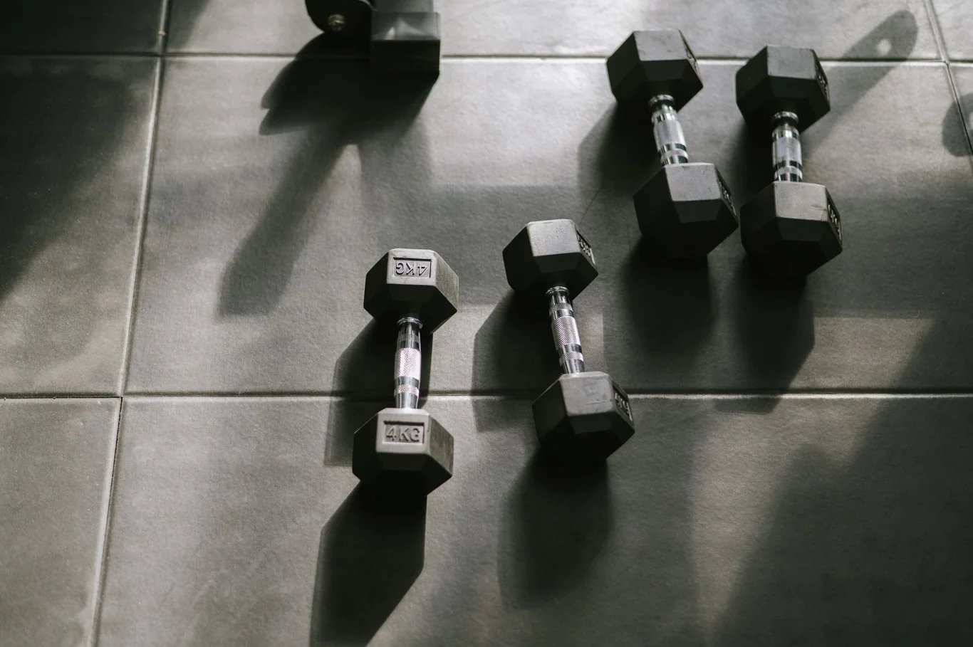 Hex dumbbells of various weights lined up on a tiled home gym floor