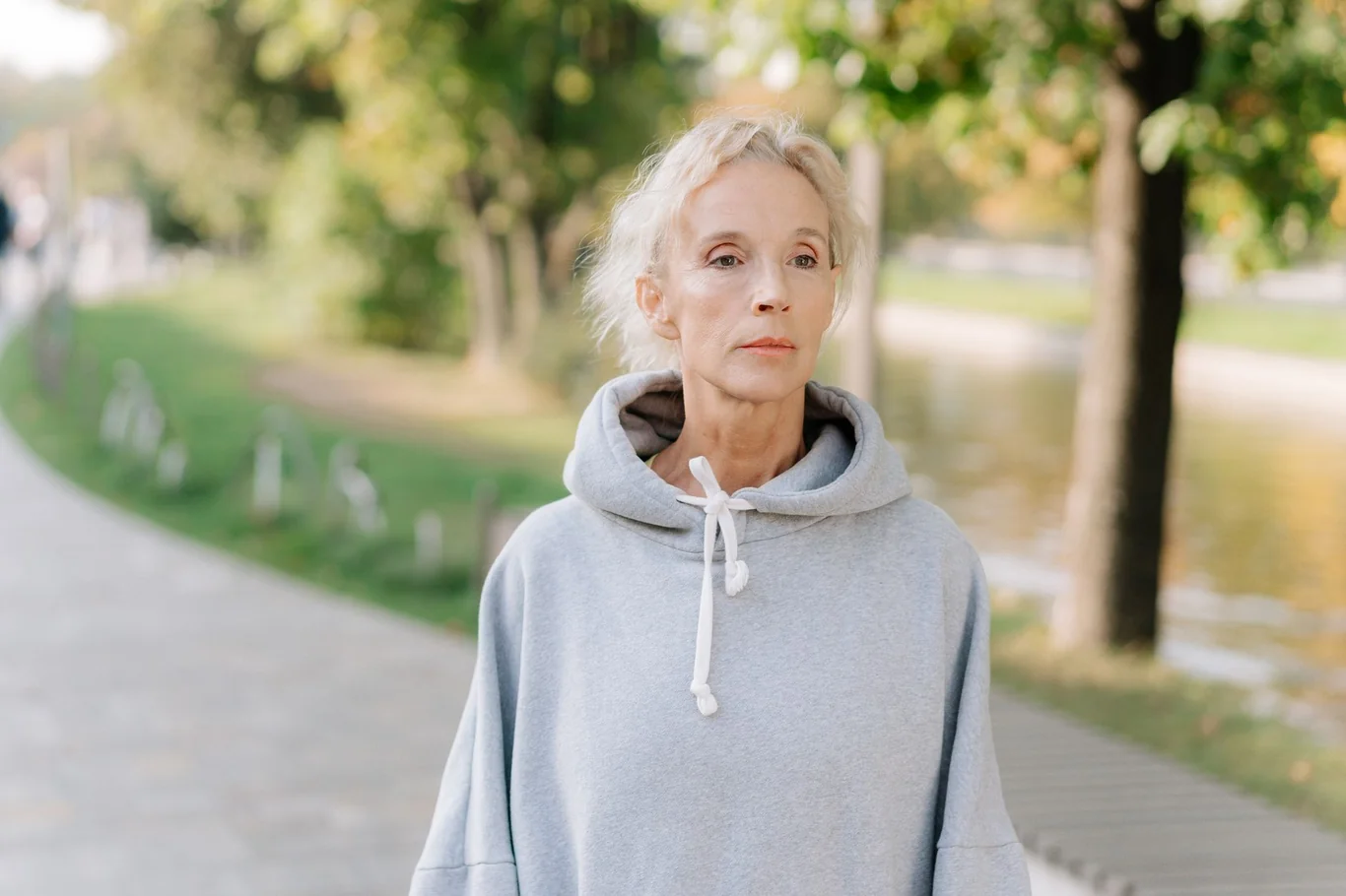 Older woman in gray hoodie walking outdoors in a park on a sunny day