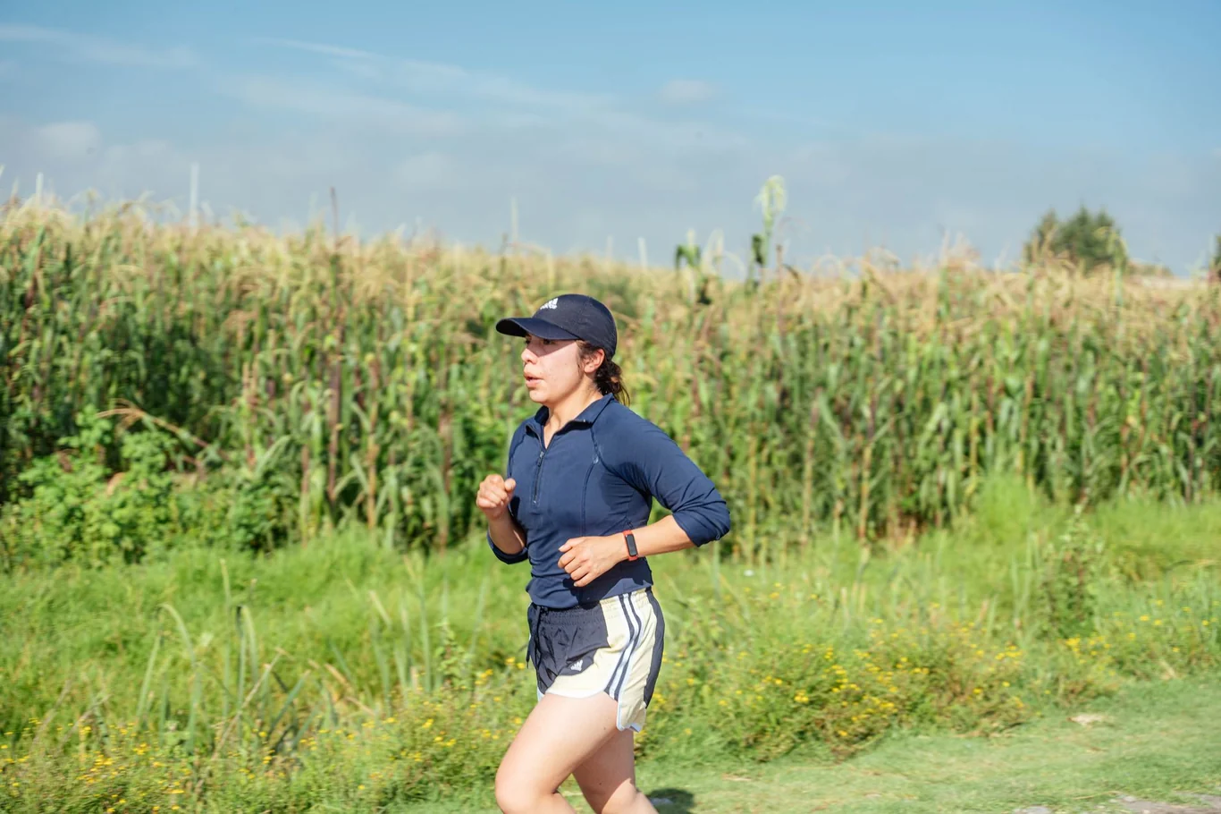 Woman jogging outdoors along a green field wearing a fitness tracker on her wrist