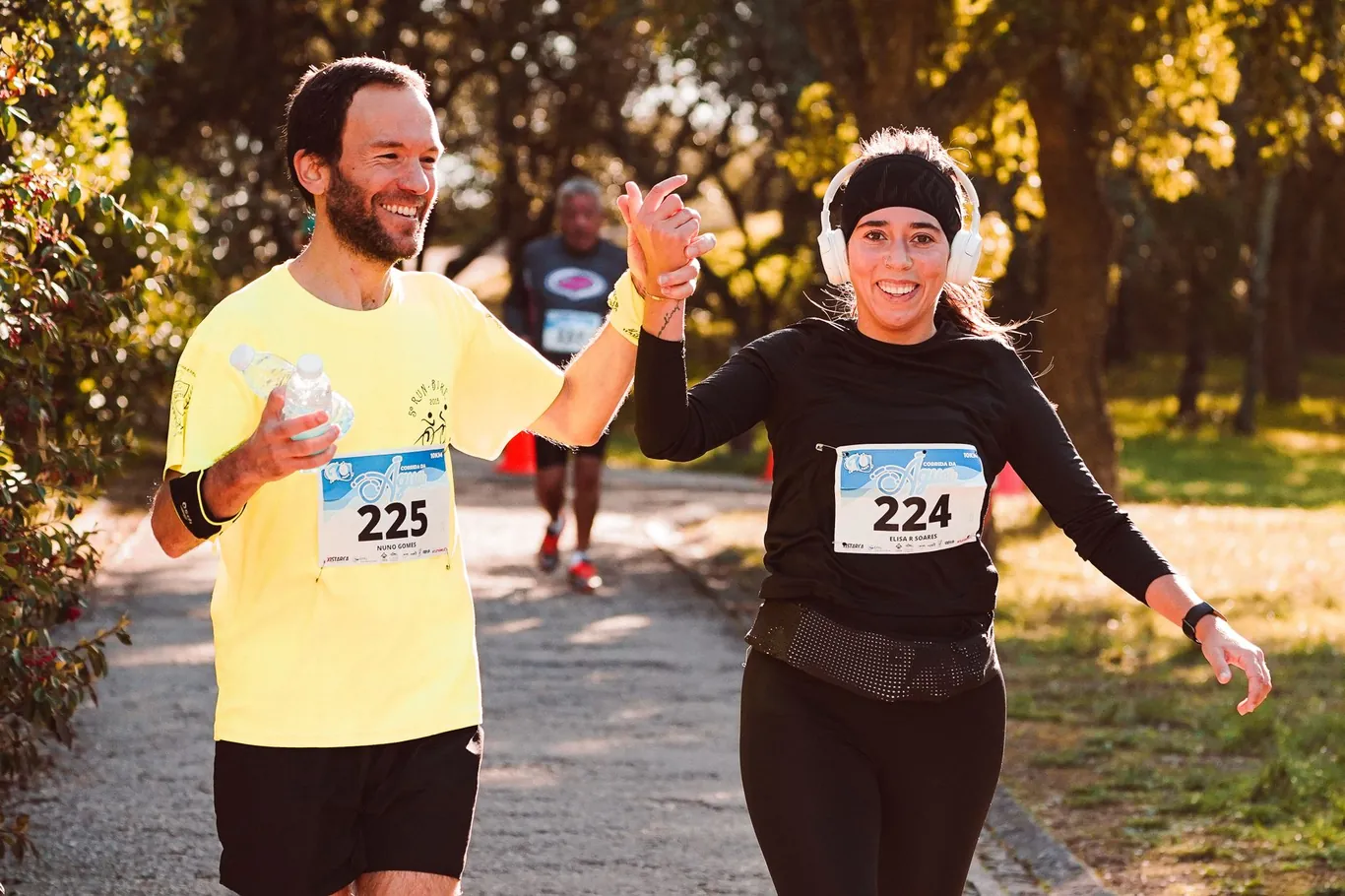 Man and woman running together outdoors during a race, smiling and high-fiving