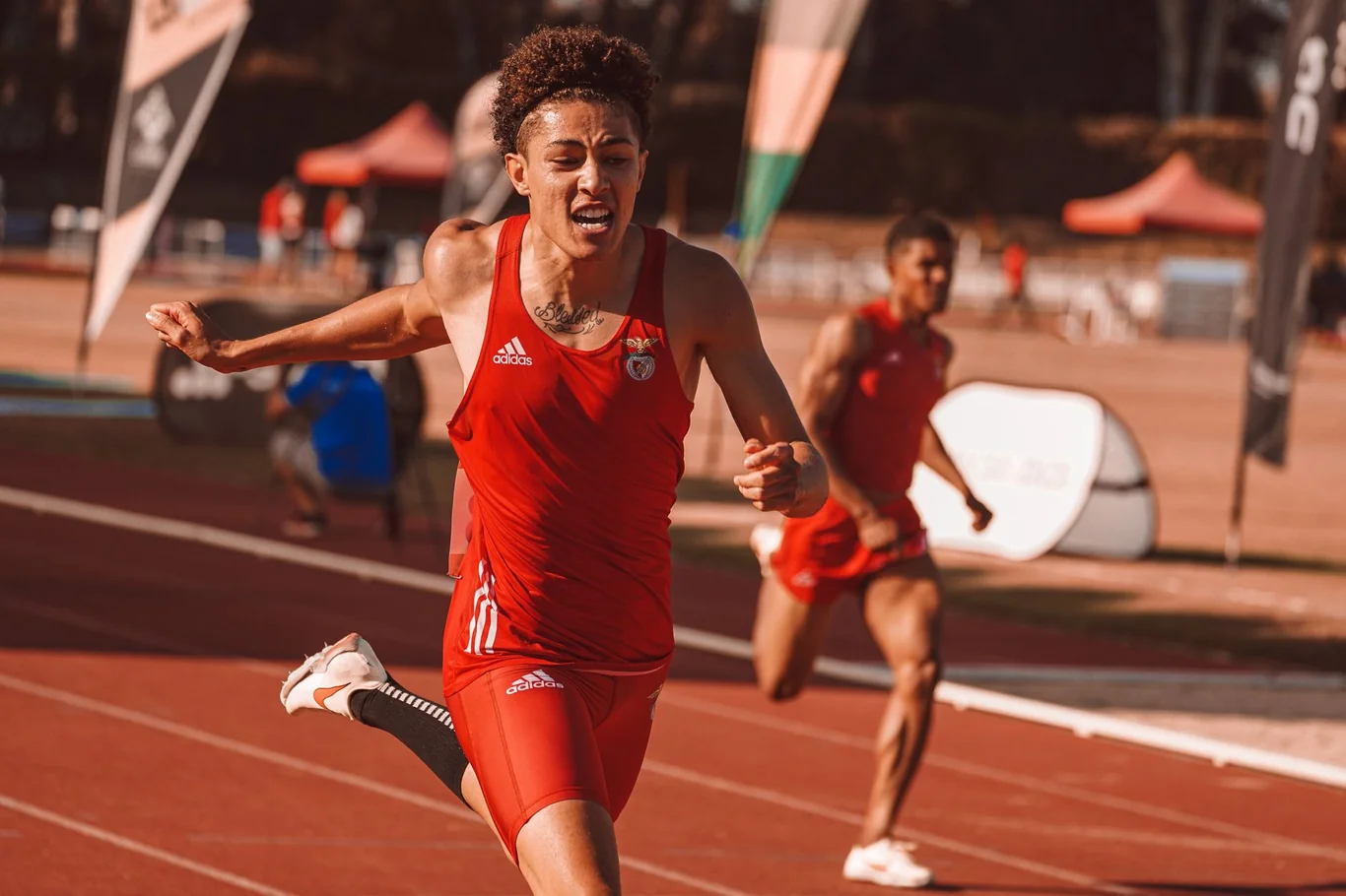 Male sprinter in red uniform running at full speed on an outdoor athletics track