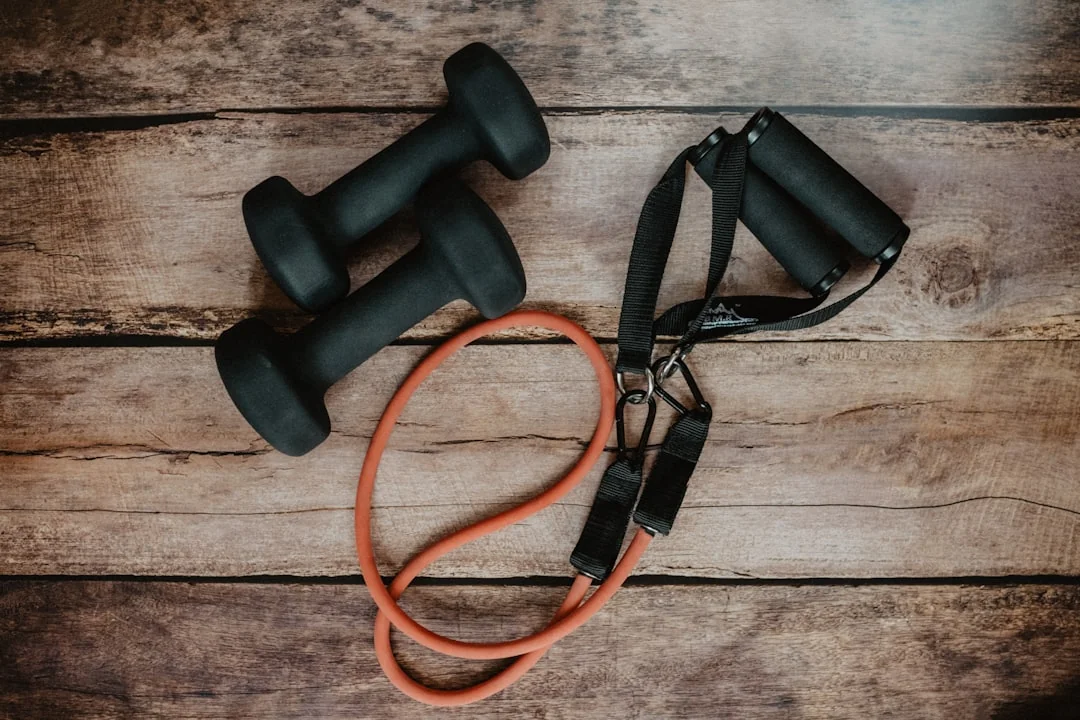 Two black dumbbells and an orange resistance band with handles on a wood floor