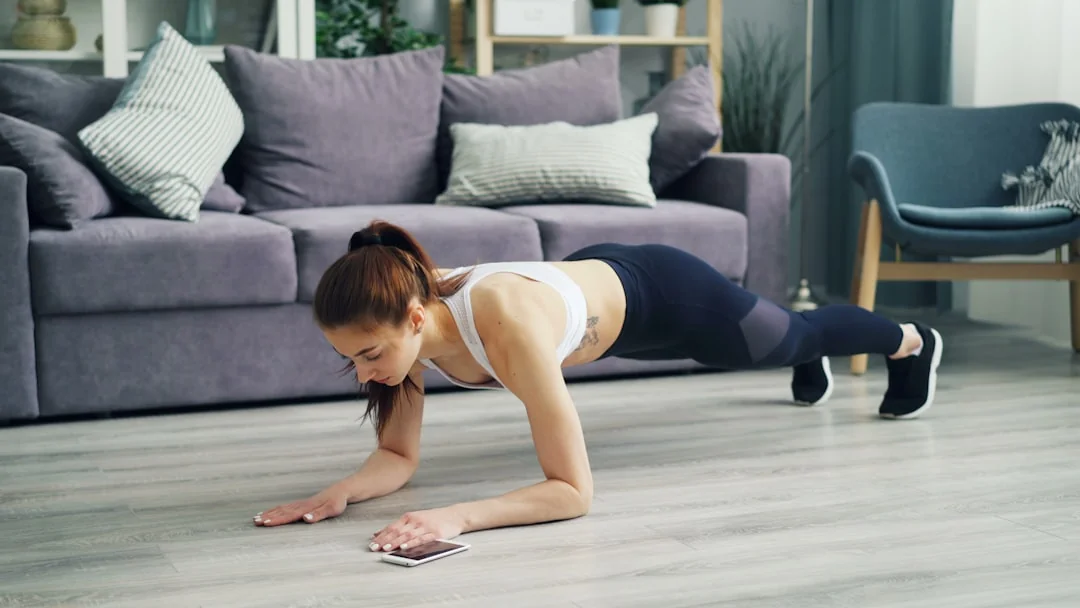 Woman holding a plank on a wood floor while checking a smartphone nearby